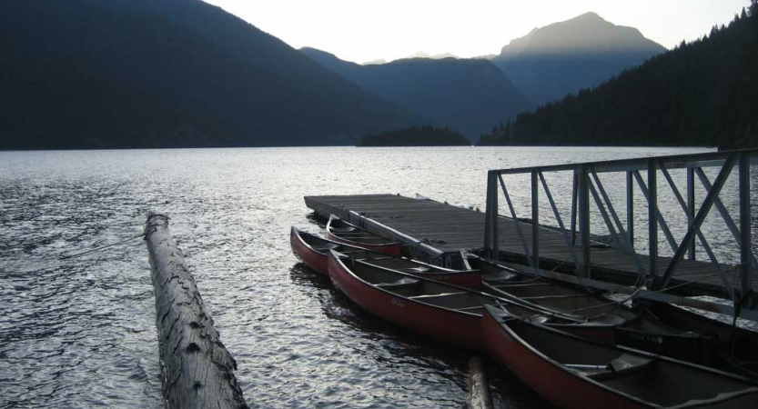 canoes rest beside a dock on a calm lake with mountains in the background